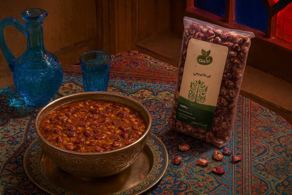 آش سنتی ایرانی پخته‌شده با لوبیا عروس در ظرف اصیل ایرانی همراه با تنگ و لیوان شیشه‌ای قدیمی و بسته‌بندی لوبیا عروس آبگینه