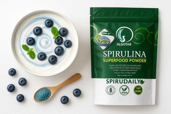 کاسه ماست وگان با سwirل آبی و بلوبری تازه کنار بسته‌بندی **پودر جلبک اسپرولینا آلگوتب باطعم بلوبری**؛ چیدمان فلت‌لی 16:9 مناسب اسموتی و ماست