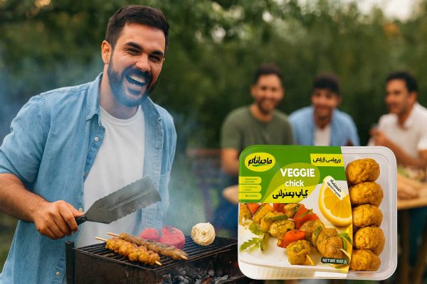 مردی خندان در حال باد زدن کباب زعفرانی گیاهی ماهانام روی منقل زغالی با گوجه، فلفل و پیاز کبابی و دوستان پسرش که پشت سر او نشسته و کباب می‌خورند