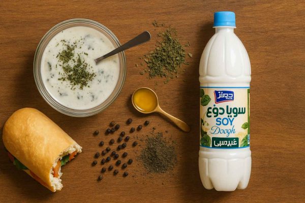 سویا دوغ هراز ۱.۵ لیتری در نمای بالا کنار سس سالاد سبک با نعناع خشک، فلفل سیاه، یک قاشق آب‌نارنج و ساندویچ گازخورده روی میز