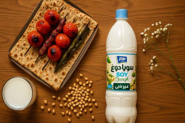 سویا دوغ هراز ۱.۵ لیتری روی میز چوب بلوط؛ کنار لیوان دوغ، دانه‌های سویا، نان سنگک با گوجه و فلفل کبابی و یک شاخه گل