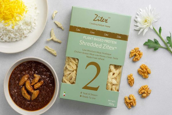 جایگزین سینه مرغ گیاهی زیتکس کنار فسنجان گیاهی با تکه‌های پخته شده محصول و پلو زعفرانی روی میز مدرن