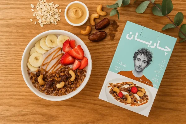 تصویر اسموتی صبحگاهی وگان با موز، توت‌فرنگی، شیر جو دوسر و گرانولا چاربان روی میز چوب سپیدار